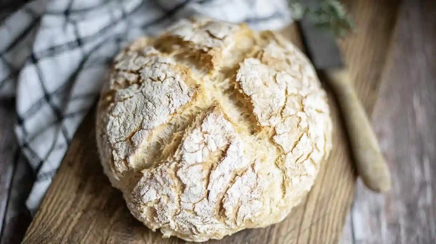Rustic round loaf from a gluten free sourdough bread recipe with a crackly golden crust and cross scoring on top, resting on a wooden cutting board