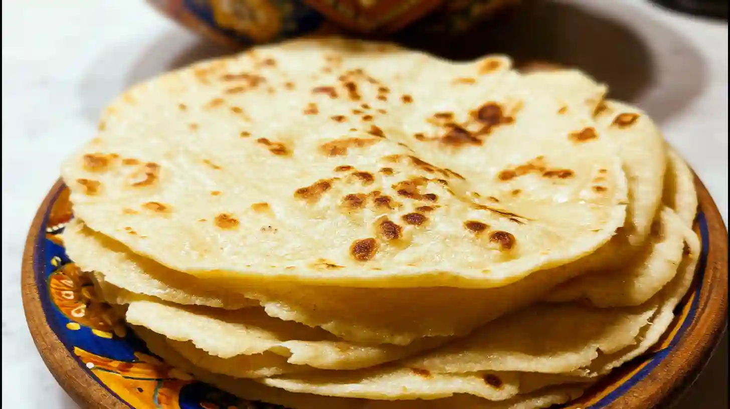 A close-up of a warm stack of soft, pliable almond flour tortillas layered on a red and gold patterned plate.