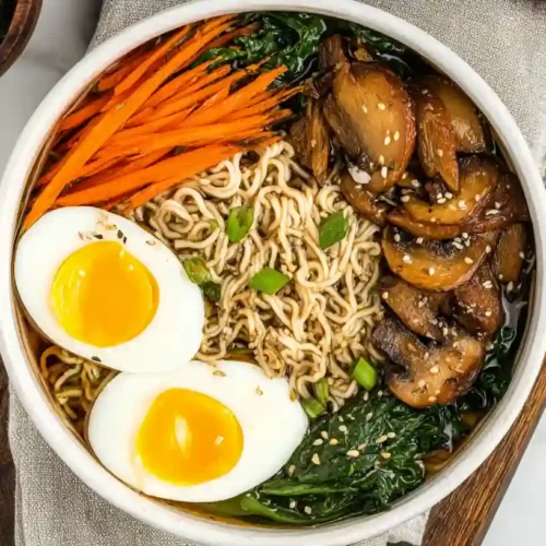 Overhead view of a delicious bowl of homemade gluten free ramen, topped with a soft-boiled egg, shredded carrots, and sautéed mushrooms.