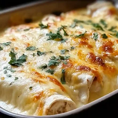 A close-up shot of cheesy baked White Chicken Enchiladas in a baking dish, with a golden brown bubbly top and a sprinkle of fresh cilantro.