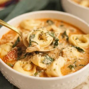 Creamy chicken tortellini soup in a white bowl with a gold spoon, garnished with spinach and Parmesan. Perfect crockpot or slow cooker recipe.