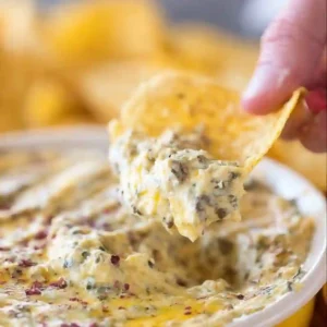 A tortilla chip scooping up a generous portion of warm Hissy Fit Dip.