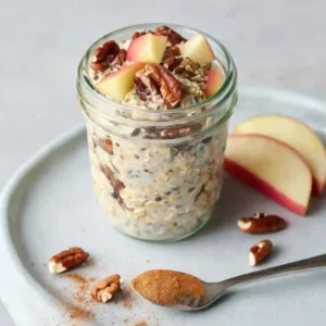 A brightly lit glass mason jar filled with layered overnight oats, topped with fresh berries, nuts, and a small wooden spoon, ready for a healthy breakfast.