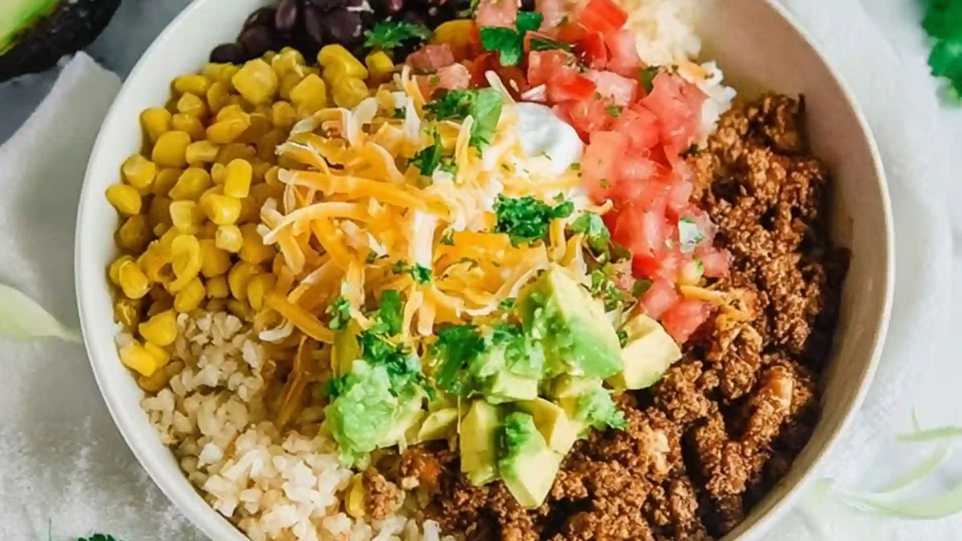 A fully assembled Taco Rice Bowl with ground beef, black beans, corn, and lime crema on a wooden table.