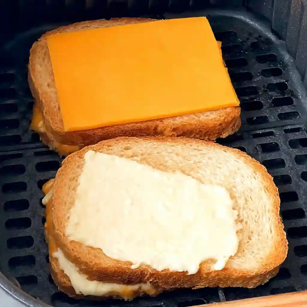 Raw grilled cheese sandwich in an air fryer basket secured with a toothpick.