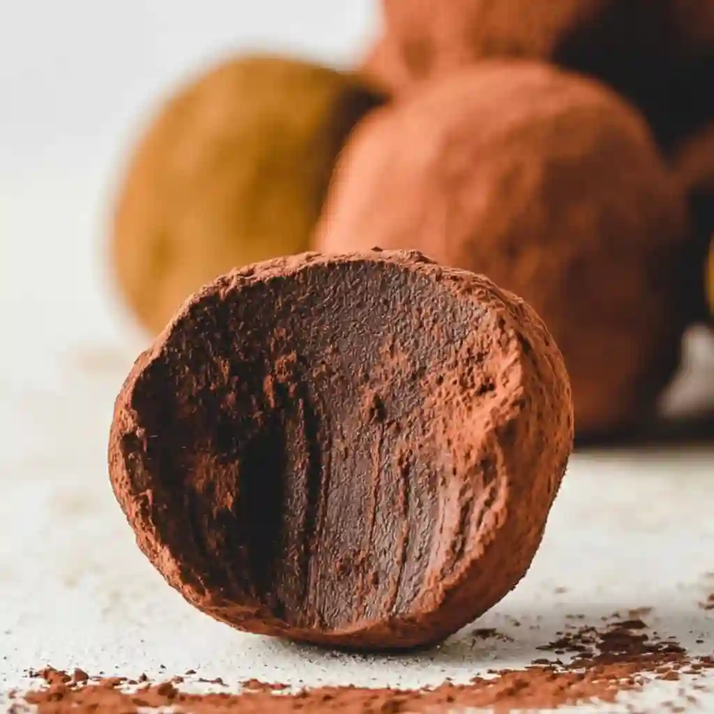 Hands rolling chocolate truffles and coating them in chopped nuts and cocoa.
