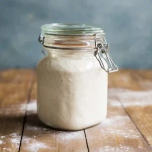 Bubbly and active sourdough starter rising in a jar showing signs of successful fermentation.