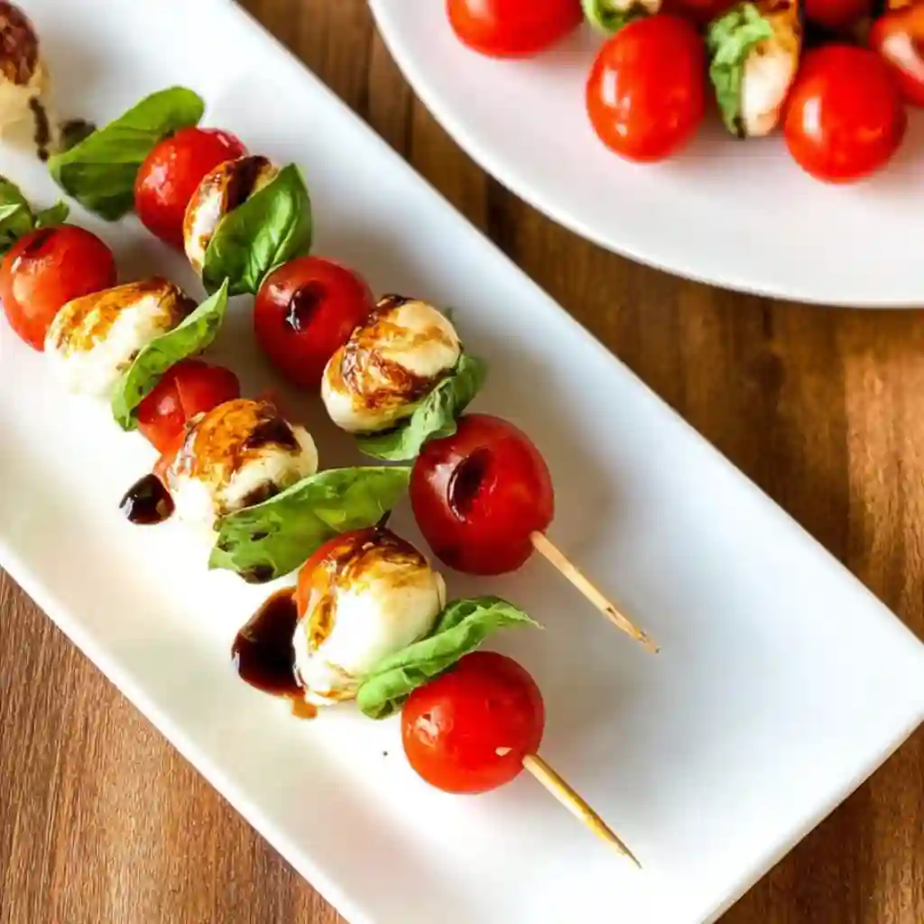Hands threading a cherry tomato and basil leaf onto a toothpick to make Caprese Skewers.
