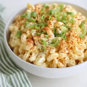 Bowl of creamy deviled egg pasta salad garnished with paprika and green onions.