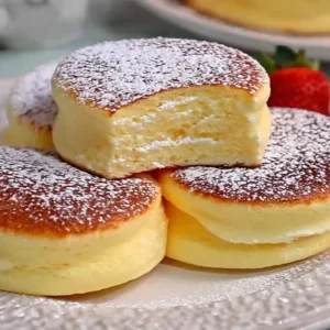 Stack of three fluffy Japanese soufflé pancakes with syrup and whipped cream.