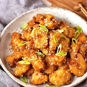 Bowl of crispy Gluten-Free Orange Chicken served over white rice with chopsticks