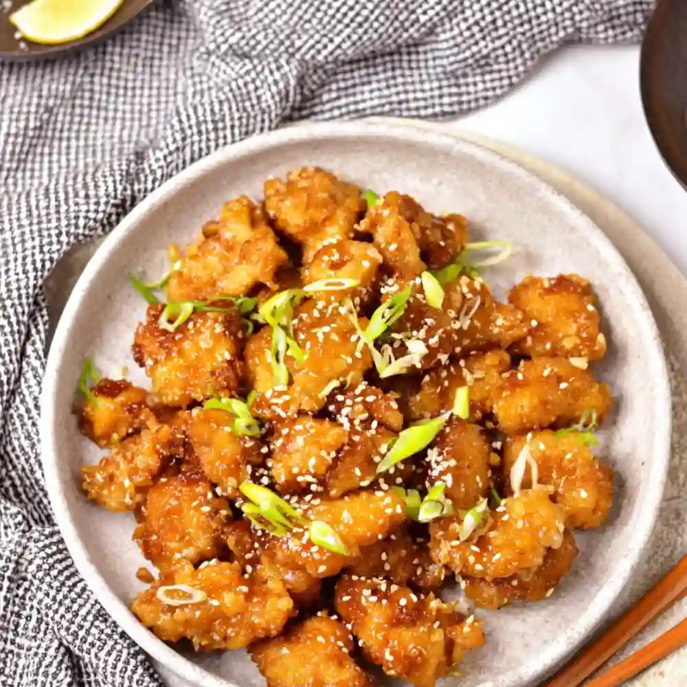 Tossed crispy chicken in sticky orange sauce in a wok.
